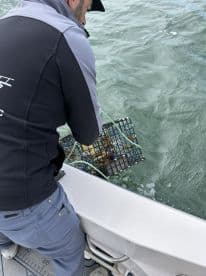 An angler actively pulling up a crab trap while fishing on a boat, showcasing the excitement of crabbing in coastal waters.