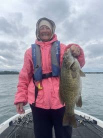 An enthusiastic angler proudly displaying a large Smallmouth Bass while fishing on a cloudy day.