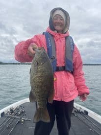 An angler proudly displaying a large Smallmouth Bass while fishing on a calm lake, showcasing a successful day on the water.