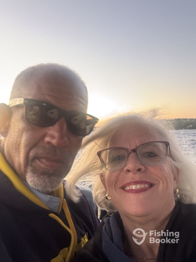 A couple enjoying a fishing trip, capturing a selfie on the boat with a scenic background.