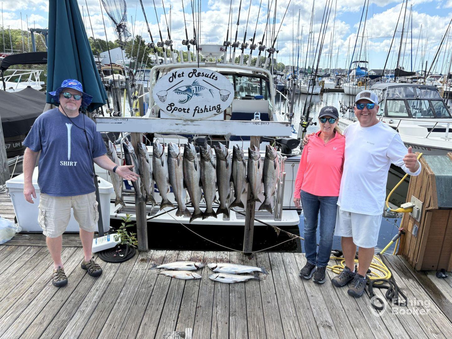 A group of anglers proudly displaying their catch of trout on a catch board at the marina, showcasing a successful day of fishing.