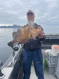 An angler proudly displaying a large Rockfish aboard a fishing boat in a scenic coastal environment.