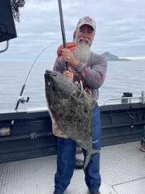 An angler proudly displaying a large Halibut while fishing on a boat in open waters.