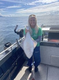 An angler proudly displaying a large Halibut aboard a fishing boat in a scenic ocean setting.