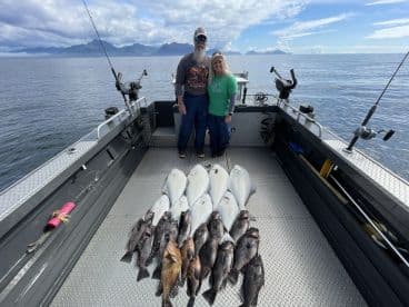Two anglers proudly displaying their catch of halibut and rockfish on a fishing boat in a scenic coastal environment.
