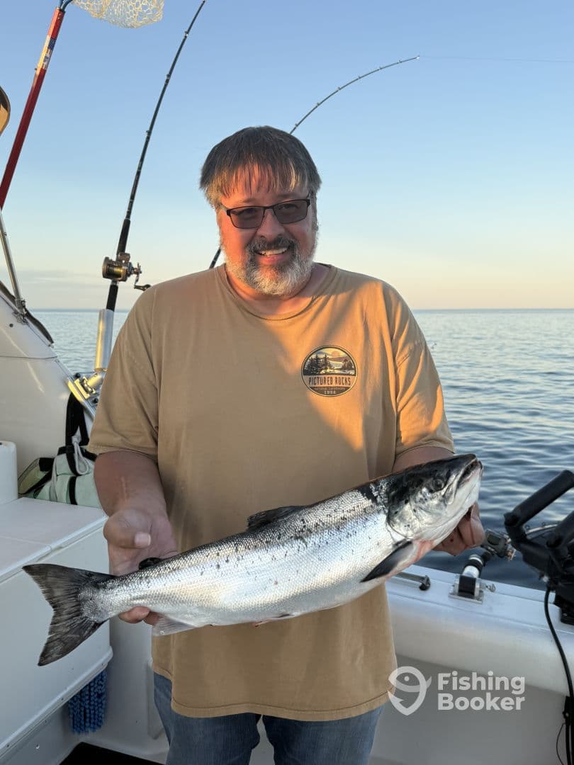 An angler proudly displaying a freshly caught Salmon while fishing on a boat during a serene sunset.