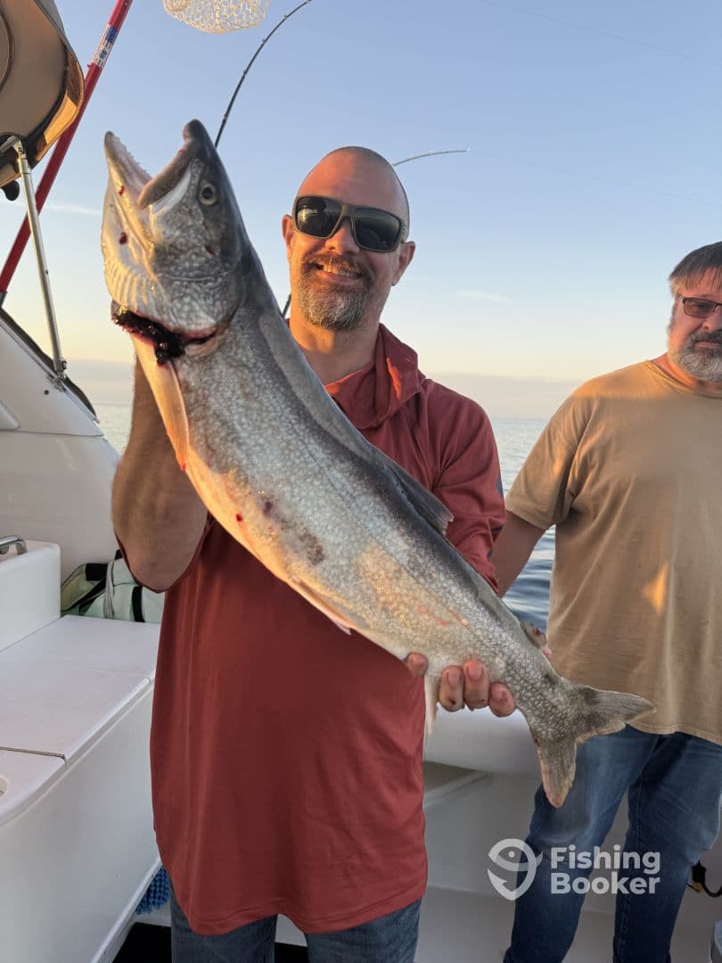An angler proudly displaying a large Lake Trout aboard a fishing boat during a sunset trip.