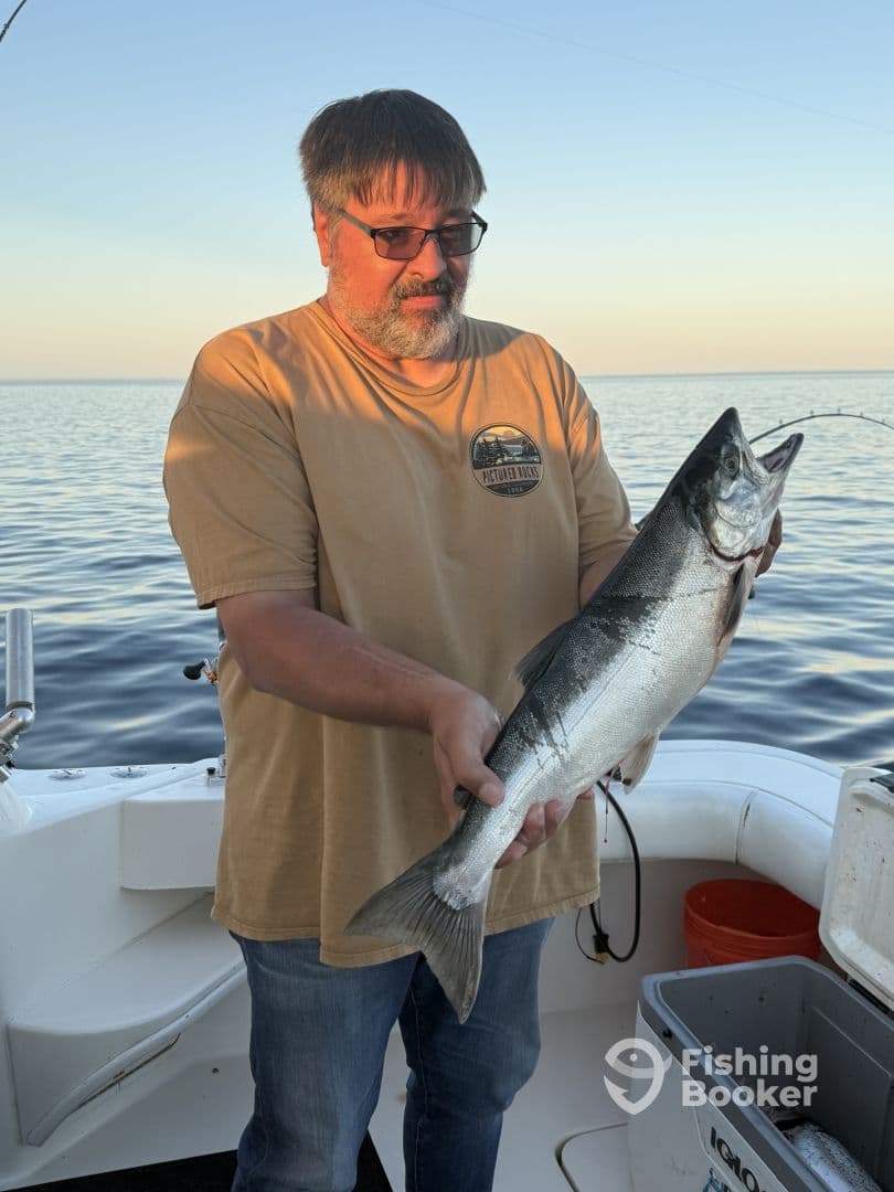 An angler proudly displaying a large Salmon on a fishing boat during a serene sunset outing.