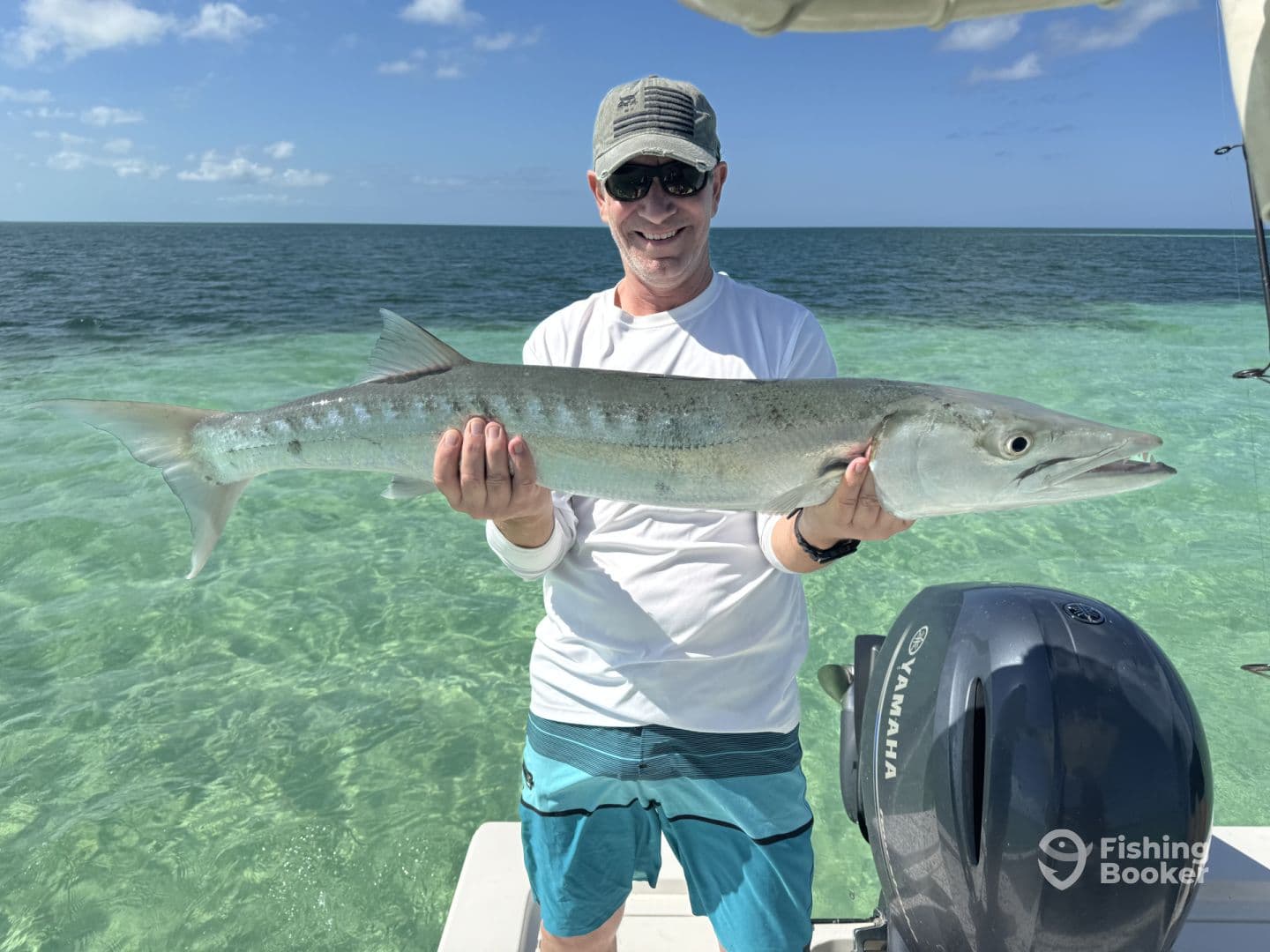 An angler proudly displaying a large Barracuda while fishing in clear waters, showcasing a successful day on the boat.