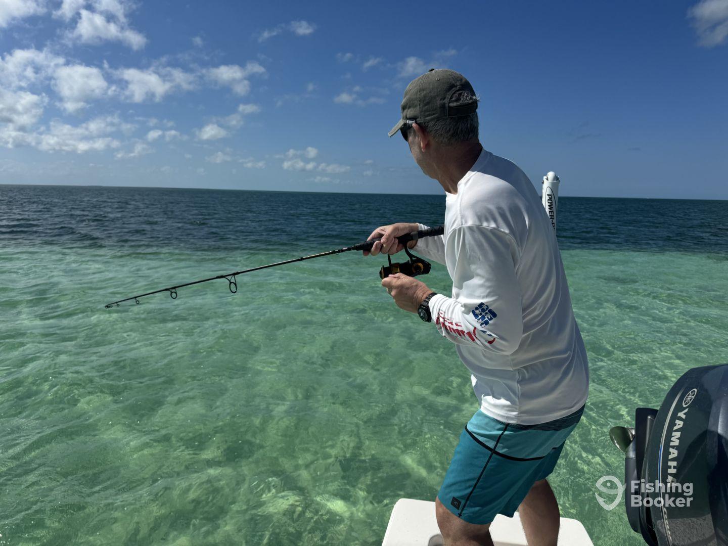 An angler casting a line into the clear waters while fishing from a boat, showcasing a beautiful day on the water.