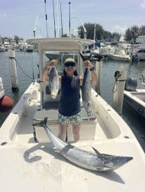 Angler proudly displaying two large fish, including a Kingfish, aboard a boat at the marina, showcasing a successful day of fishing.