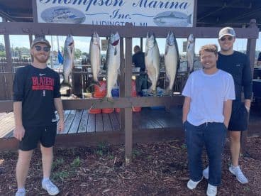 Three anglers proudly posing with their catch of Salmon displayed on a board at Thompson Marina in Ludington, MI.