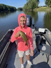 A young angler proudly displaying a Smallmouth Bass while fishing on a serene river, showcasing a perfect day for family fishing.