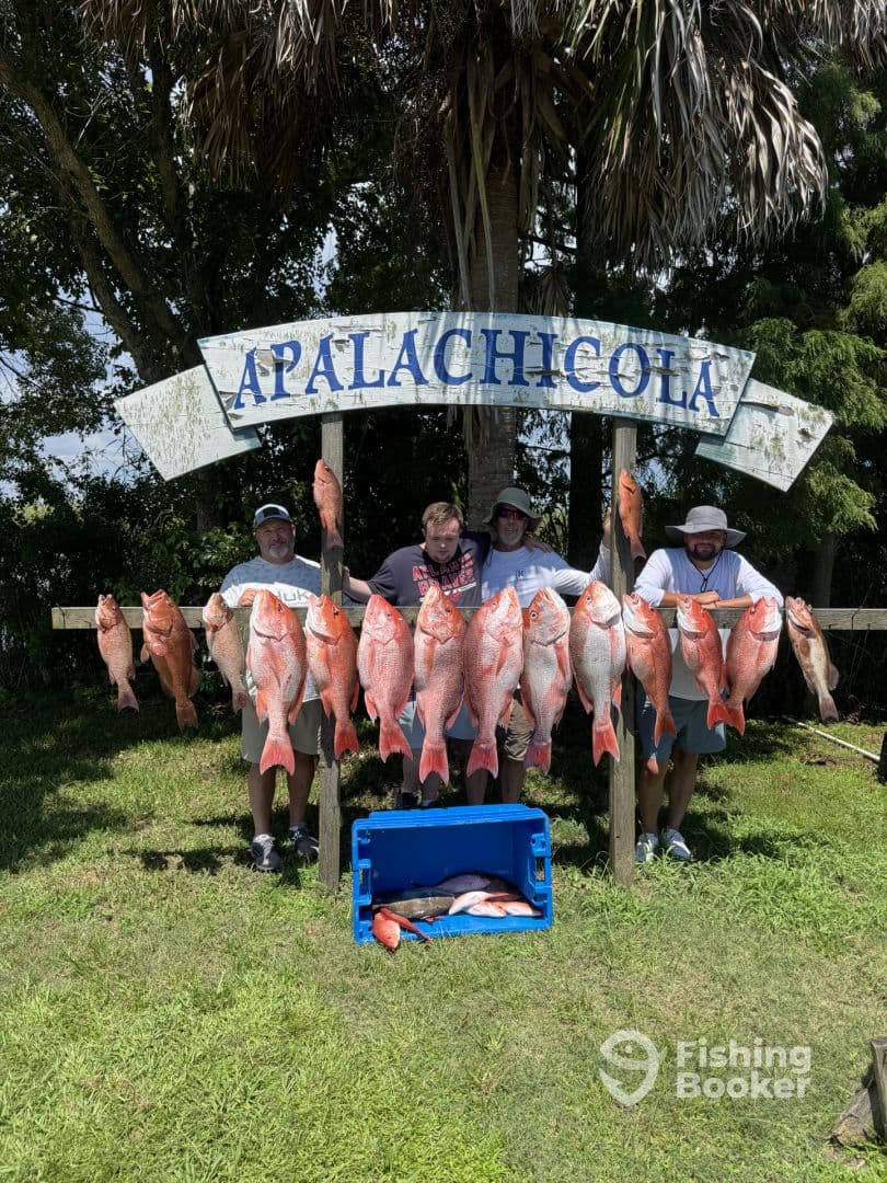 A group of anglers proudly displaying their catch of Red Snapper in Apalachicola, with a cooler of additional fish nearby.