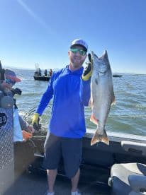 An angler proudly displaying a large Salmon while fishing on a sunny day, with other boats visible in the background.