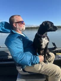 A relaxed angler enjoying a day on the water with his dog, seated comfortably in the boat's helm area.