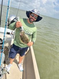 An angler proudly displaying a Flounder while fishing on a boat in coastal waters.