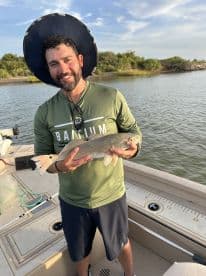 Angler proudly displaying a Redfish while standing on a boat in a scenic fishing environment.