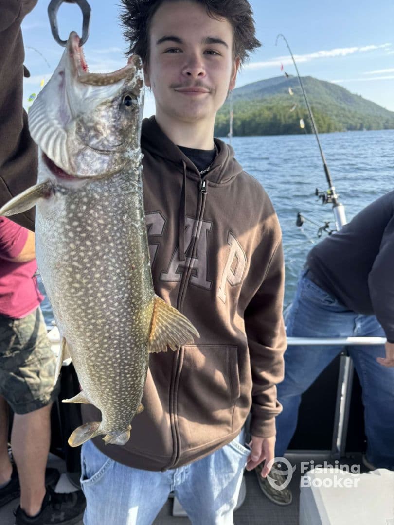 A young angler proudly displaying a freshly caught Lake Trout while fishing on a scenic lake.