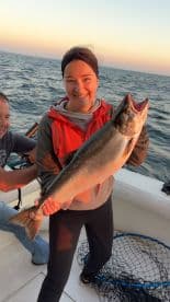 A proud angler displaying a large Salmon while fishing on a boat during sunset.
