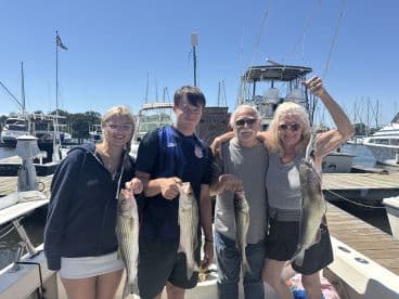A family proudly displaying their catch of striped bass and catfish aboard a boat at the marina.
