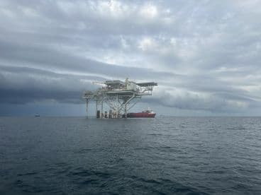 A scenic view of an offshore oil rig with a support vessel nearby, set against a dramatic sky, showcasing the fishing environment.
