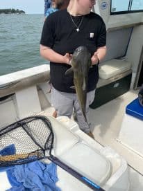 An angler proudly displaying a large catfish aboard a fishing boat, showcasing a successful day on the water.