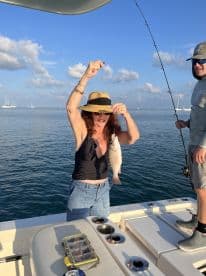 An adult angler proudly displaying a freshly caught Snapper while fishing on a boat in calm waters.