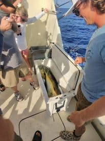 A group of anglers gathered on a boat, admiring their catch of Mahi Mahi stored in a cooler, showcasing a successful offshore fishing trip.
