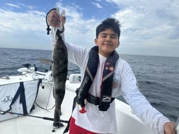 A young angler proudly displaying a large fish while fishing on a boat, showcasing a fun day out on the water.