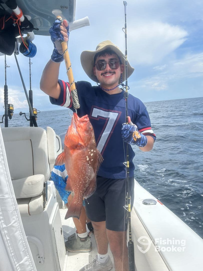An angler proudly displaying a large Red Grouper while fishing on a boat in open waters.
