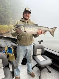 Angler proudly displaying a large Salmon while fishing in a misty environment, showcasing a successful day on the water.