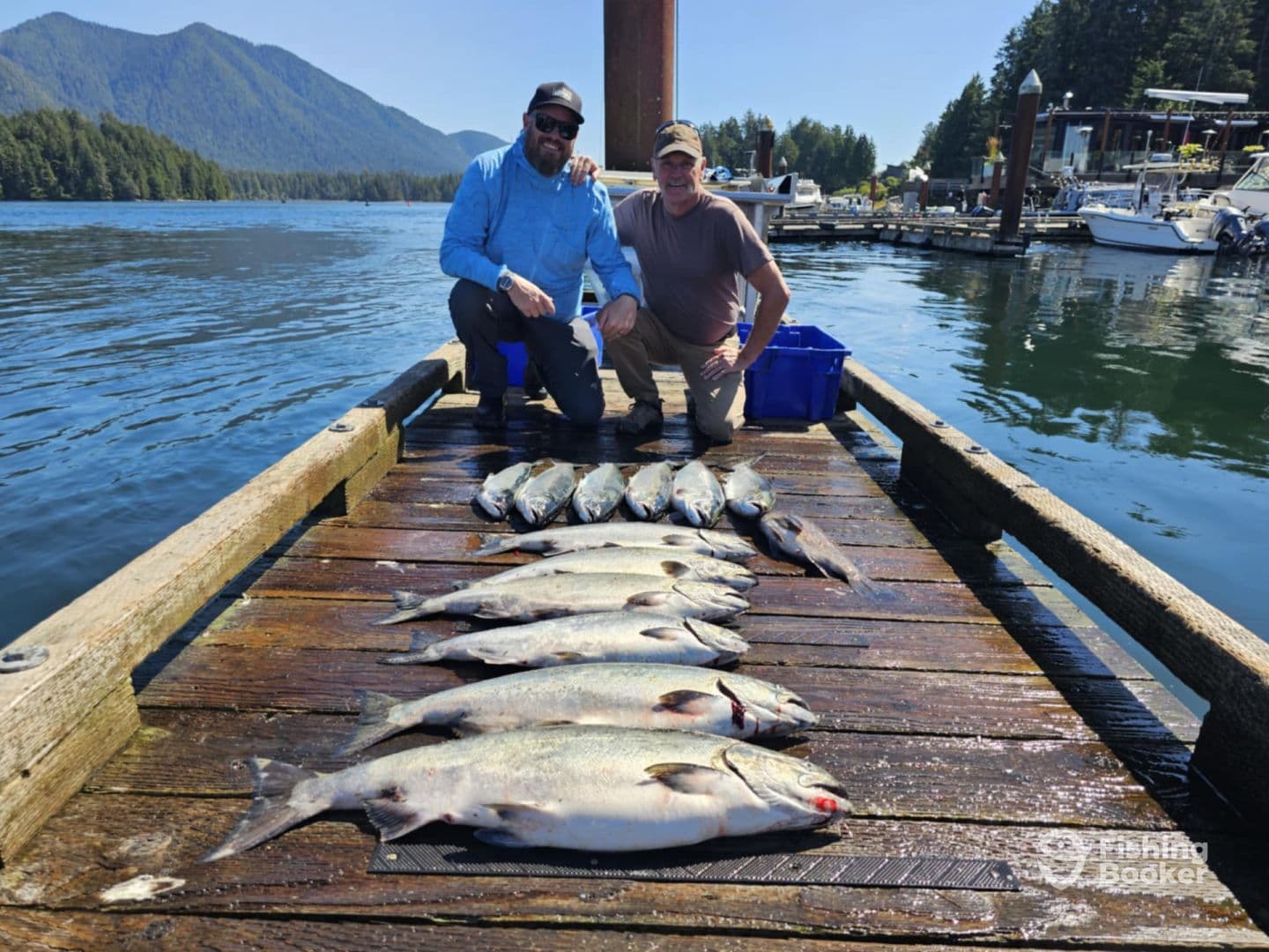 Two anglers posing with a successful catch of multiple salmon on a sunny day at the dock, showcasing their haul after a fishing trip.