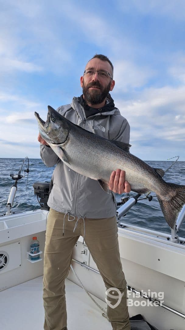 An angler proudly displaying a large Chinook Salmon aboard a fishing boat, showcasing a successful day on the water.