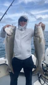 Angler proudly displaying two large striped bass while fishing on a boat, showcasing a successful day on the water.