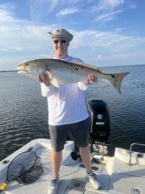 Angler proudly displaying a large Redfish while fishing on a boat in calm waters.