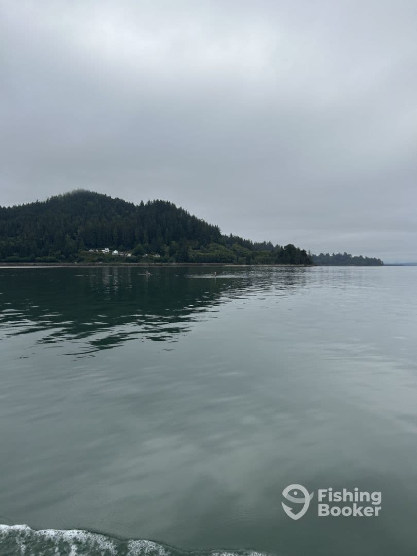 A serene view of a fishing boat on calm waters, surrounded by lush green hills and overcast skies, showcasing the tranquil fishing environment.