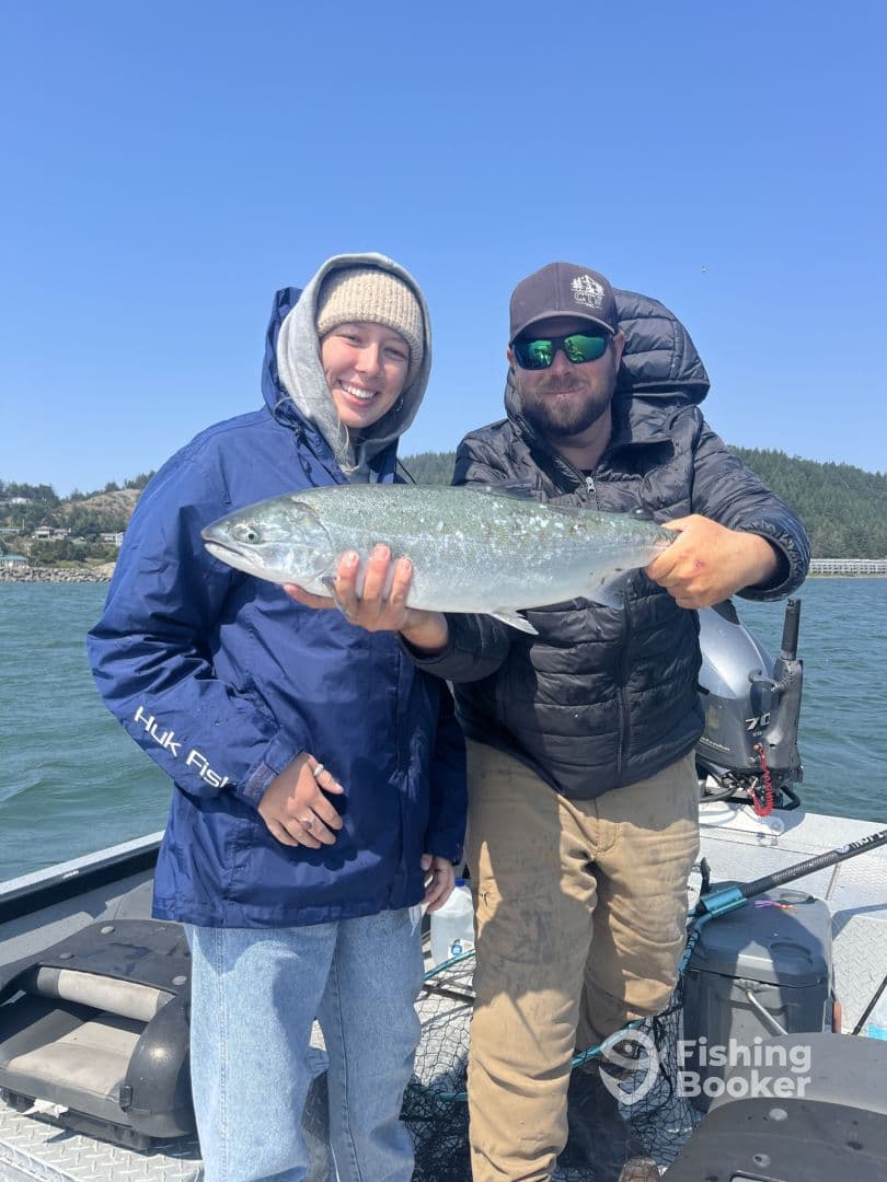 Two anglers proudly displaying a large Silver Salmon on a fishing boat, enjoying a sunny day on the water.