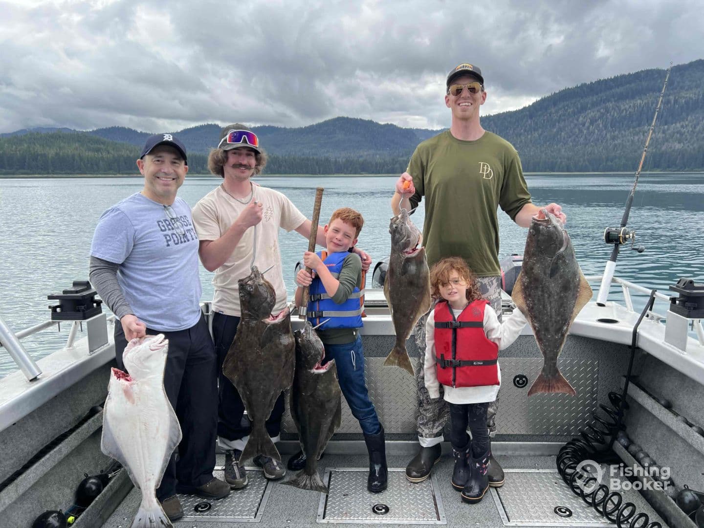 A family group proudly displaying their catch of halibut on a fishing trip in a scenic coastal environment.