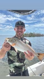 Angler proudly displaying a Redfish while fishing in a scenic waterway.