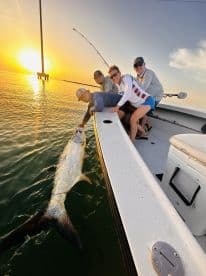 Group of anglers actively reeling in a large Tarpon during a sunset fishing trip, showcasing the excitement of sport fishing.