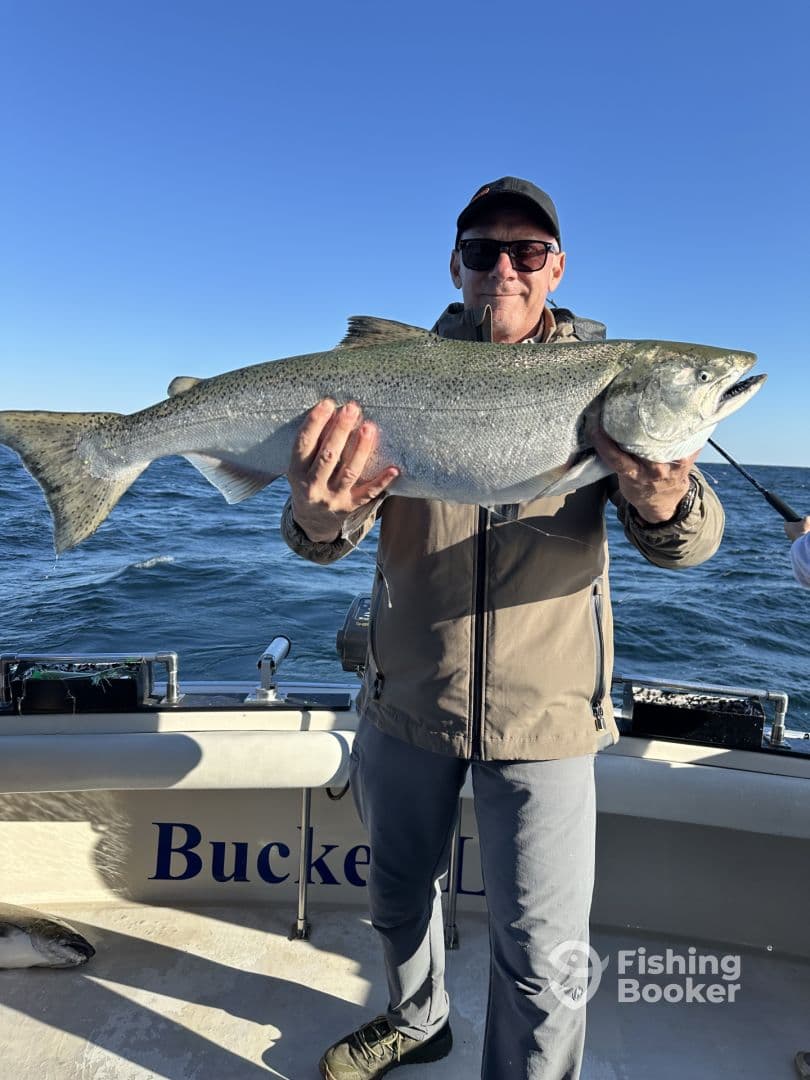 An angler proudly displaying a large Chinook Salmon while fishing on a charter boat.