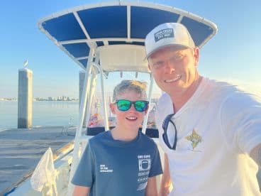 A father and son smiling together inside a boat, ready for a fishing adventure on calm waters.