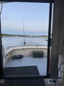 View from the interior of a fishing boat looking out towards the calm waters and nearby marina, showcasing the boat's spacious layout.