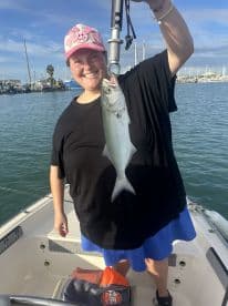 An excited angler proudly displaying a caught fish while aboard a boat in a marina setting.