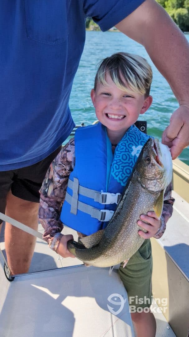 A young angler proudly displaying a Lake Trout while fishing on a sunny day.