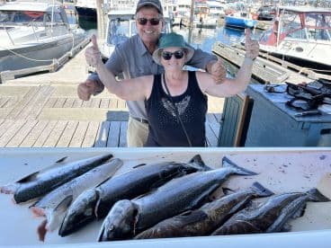 Two happy anglers posing with their catch of multiple salmon at the dock, showcasing a successful fishing trip.