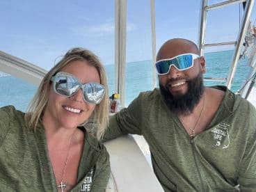 Two smiling individuals enjoying their time aboard a boat, showcasing a relaxed atmosphere with a scenic ocean backdrop.