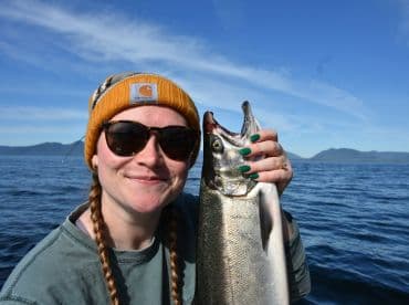 An angler proudly displaying a freshly caught fish while enjoying a sunny day on the water, with mountains in the background.