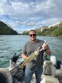 An angler proudly displaying a Walleye caught while fishing from a Lund boat in a scenic river setting.